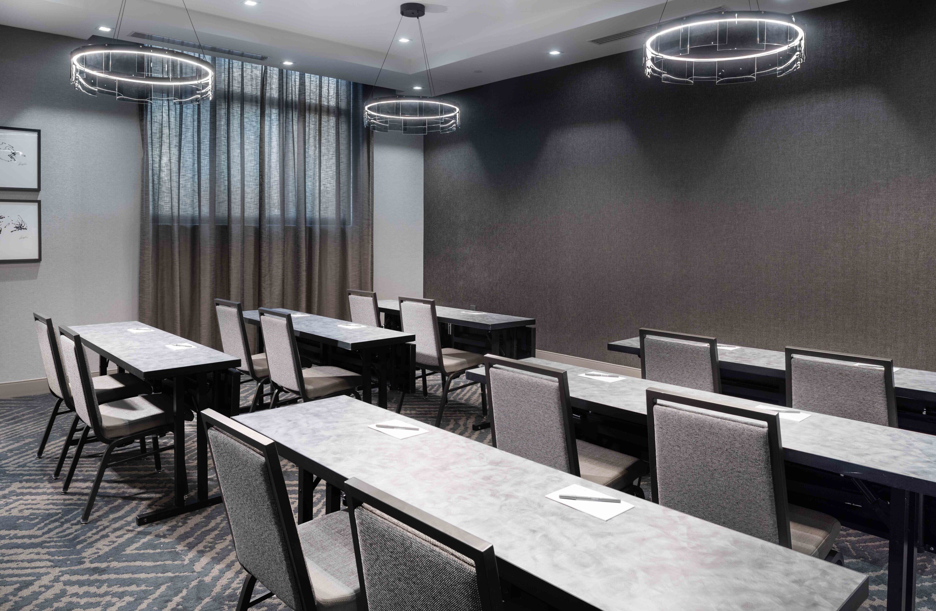 A conference room with multiple tables and chairs, large windows with curtains, and modern lighting fixtures.