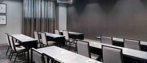 A conference room with multiple tables and chairs, large windows with curtains, and modern lighting fixtures.