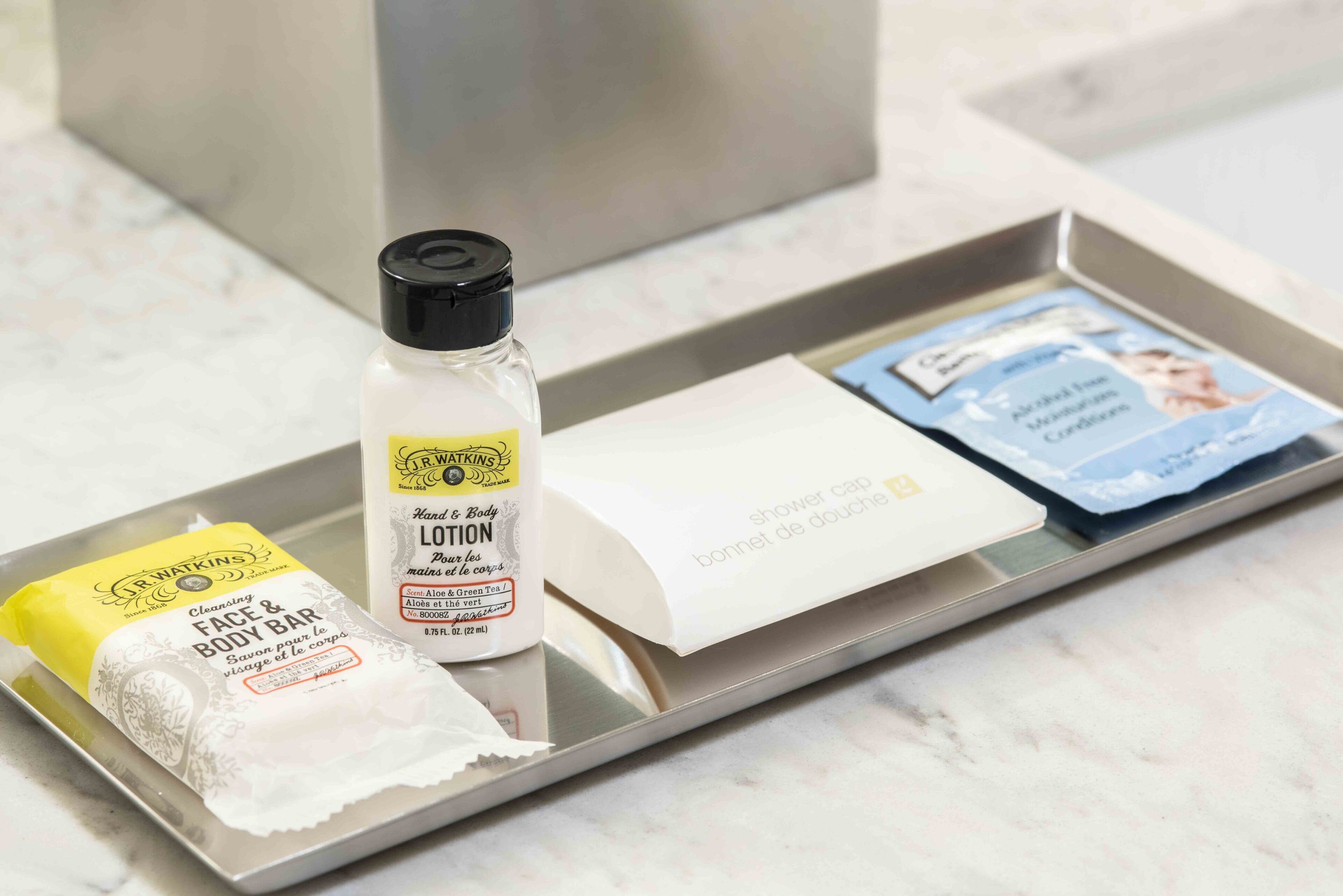 A tray with a J.R. Watkins lotion bottle, a bar of soap, and a shower cap.