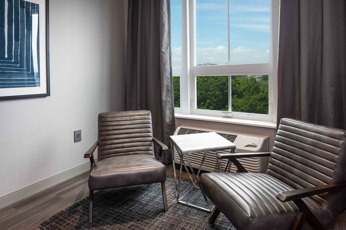 A corner room with two leather chairs, a small table, and a window with a view of greenery.