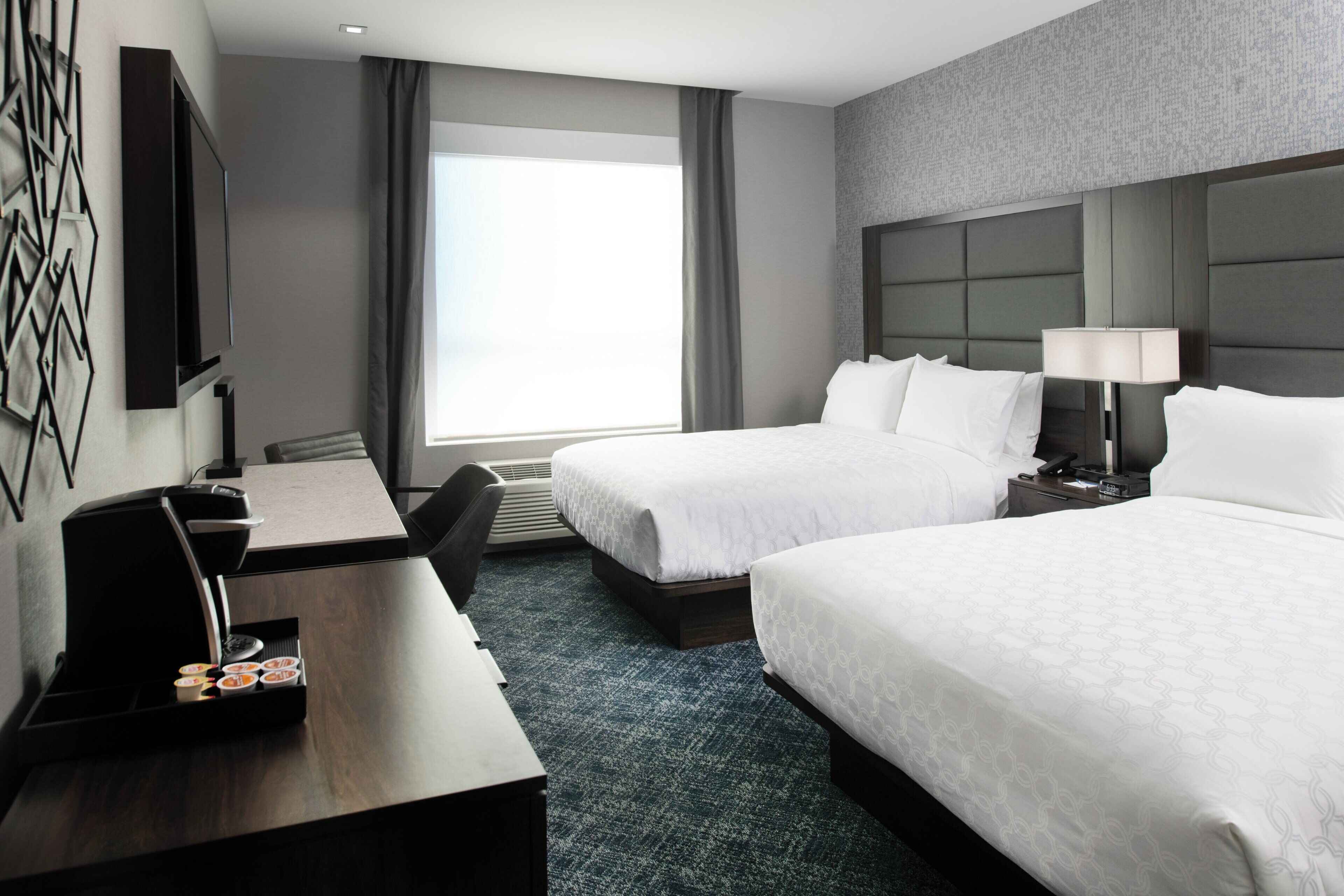 A hotel room with two beds, a desk, a chair, a TV, and a window with curtains.