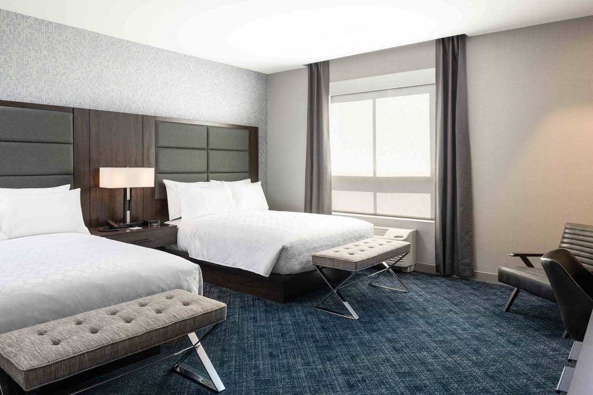 A hotel room with two beds, a desk, a chair, and a large window with curtains.