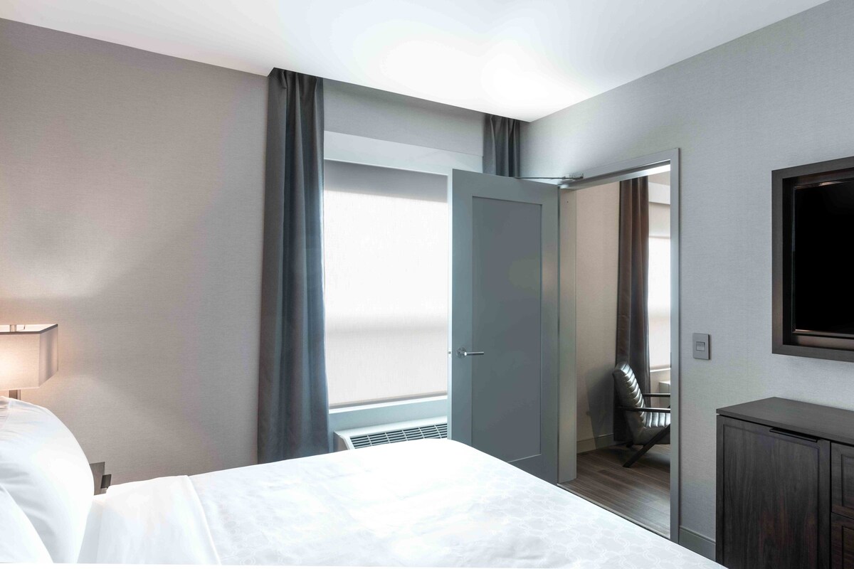 A hotel room with a bed, a desk, a chair, a TV, and a door leading to a balcony.