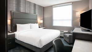 A modern hotel room with a large bed, a desk with a flat-screen TV, a chair, a desk lamp, and a window with blinds. - Holiday Inn Express Boston South - Quincy by IHG (Quincy)