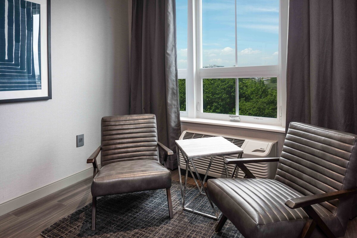 A room with two leather chairs, a small table, and a window with a view of greenery.