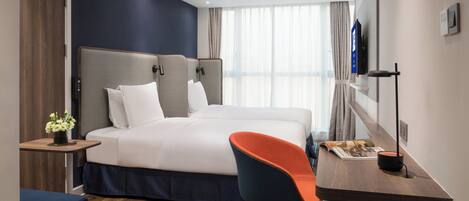 Ein Hotelzimmer mit einem Bett, einem Schreibtisch mit Stuhl, einem Fernseher und einem Fenster mit Vorhängen.