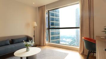 A modern living room with a sofa, a round coffee table, a lamp, and a view of a cityscape through large windows.