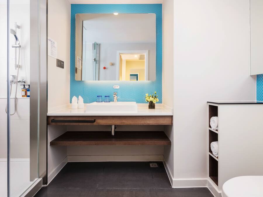 A modern bathroom with a glass shower enclosure, a white sink with a blue backsplash, and a mirror above the sink.