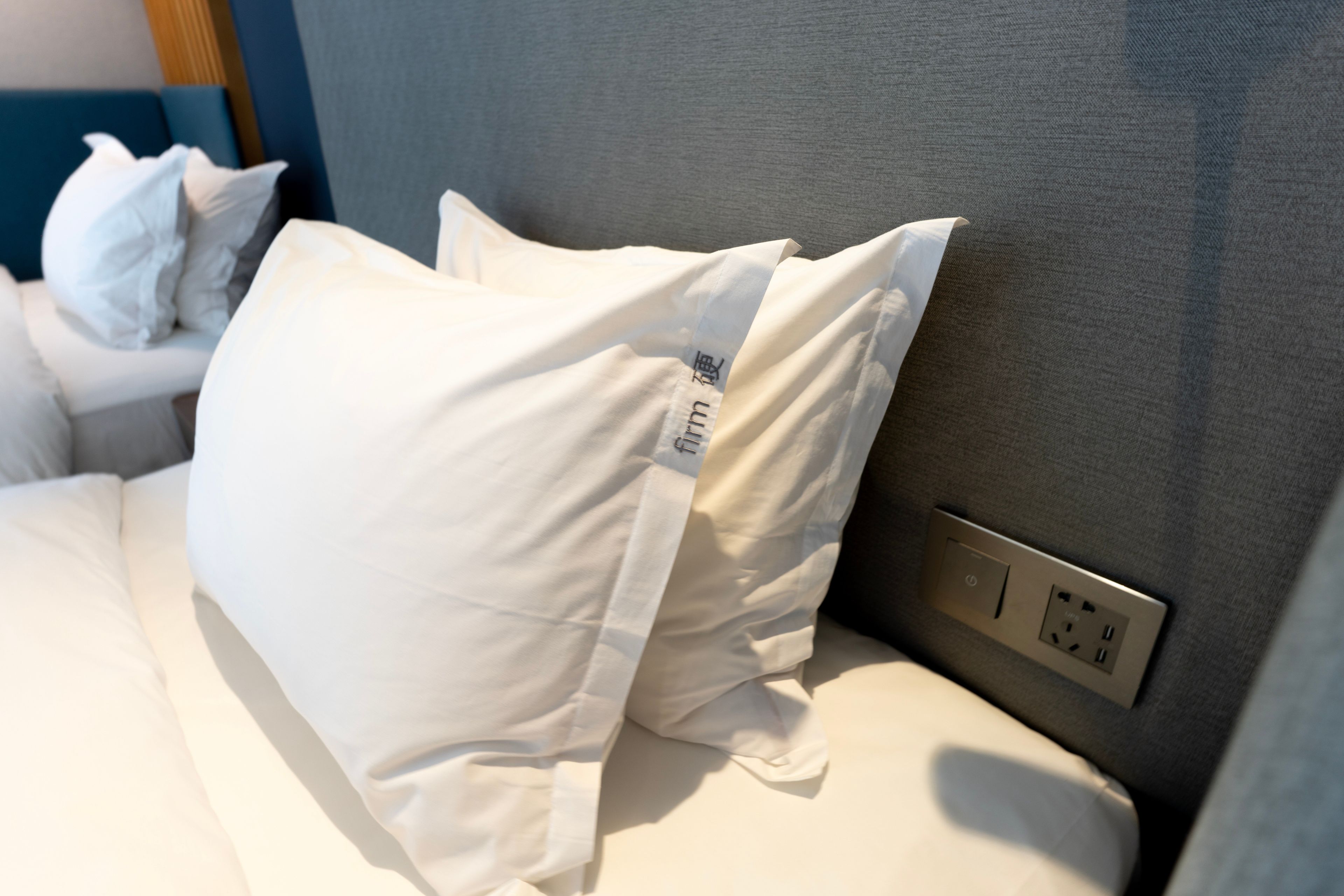 A bed with white bedding and a visible power outlet on the headboard.