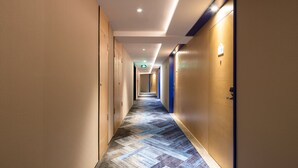 A hotel hallway with a patterned carpet, doors on both sides, and recessed lighting on the ceiling.