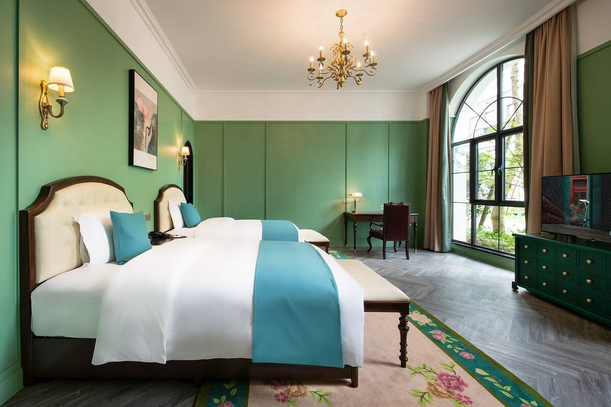 A bedroom with a bed, a desk, a chair, a television, and a window with curtains.