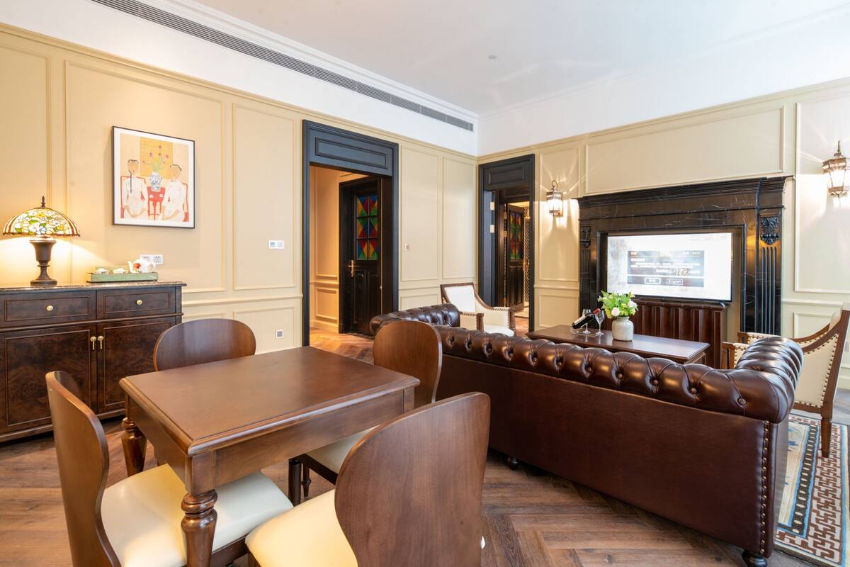 A traditional room with a dining table, leather sofa, and a fireplace.