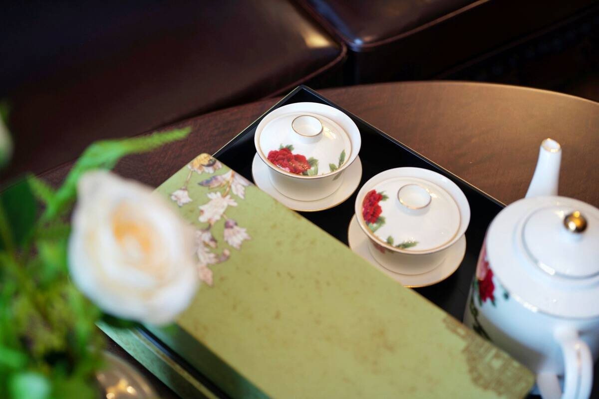 A table with a floral tablecloth, a teapot, and two cups with floral designs.