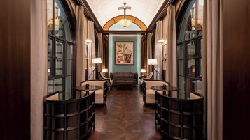 A hallway with a central seating area, flanked by two tables with lamps, leading to a room with a large painting.