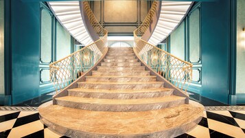 A grand staircase with marble steps and golden railings, leading to a landing with a large window.