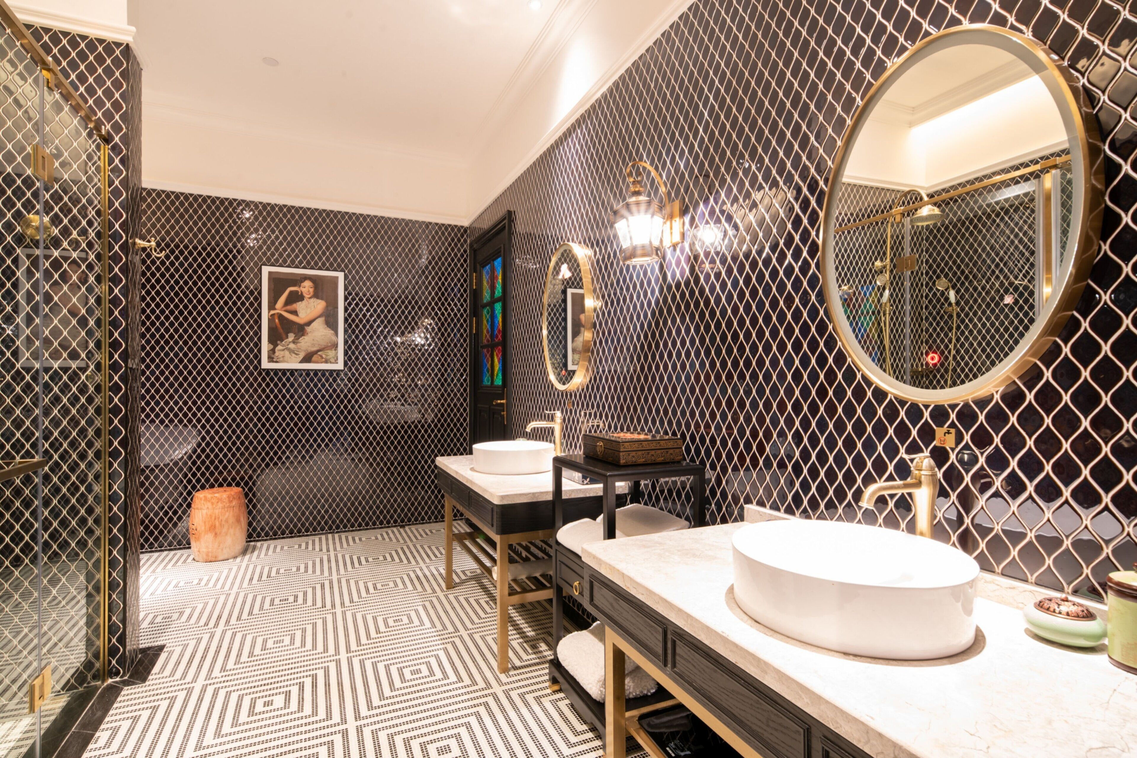 Une salle de bain moderne avec un carrelage au motif géométrique, un grand miroir rond et deux vasques.