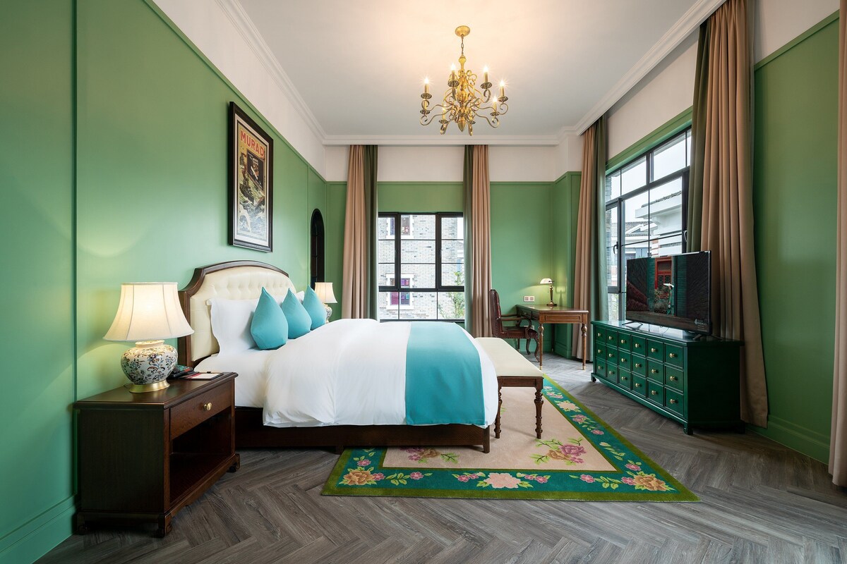 Een hotelkamer met een groot bed, een kroonluchter, een televisie en uitzicht op de stad.