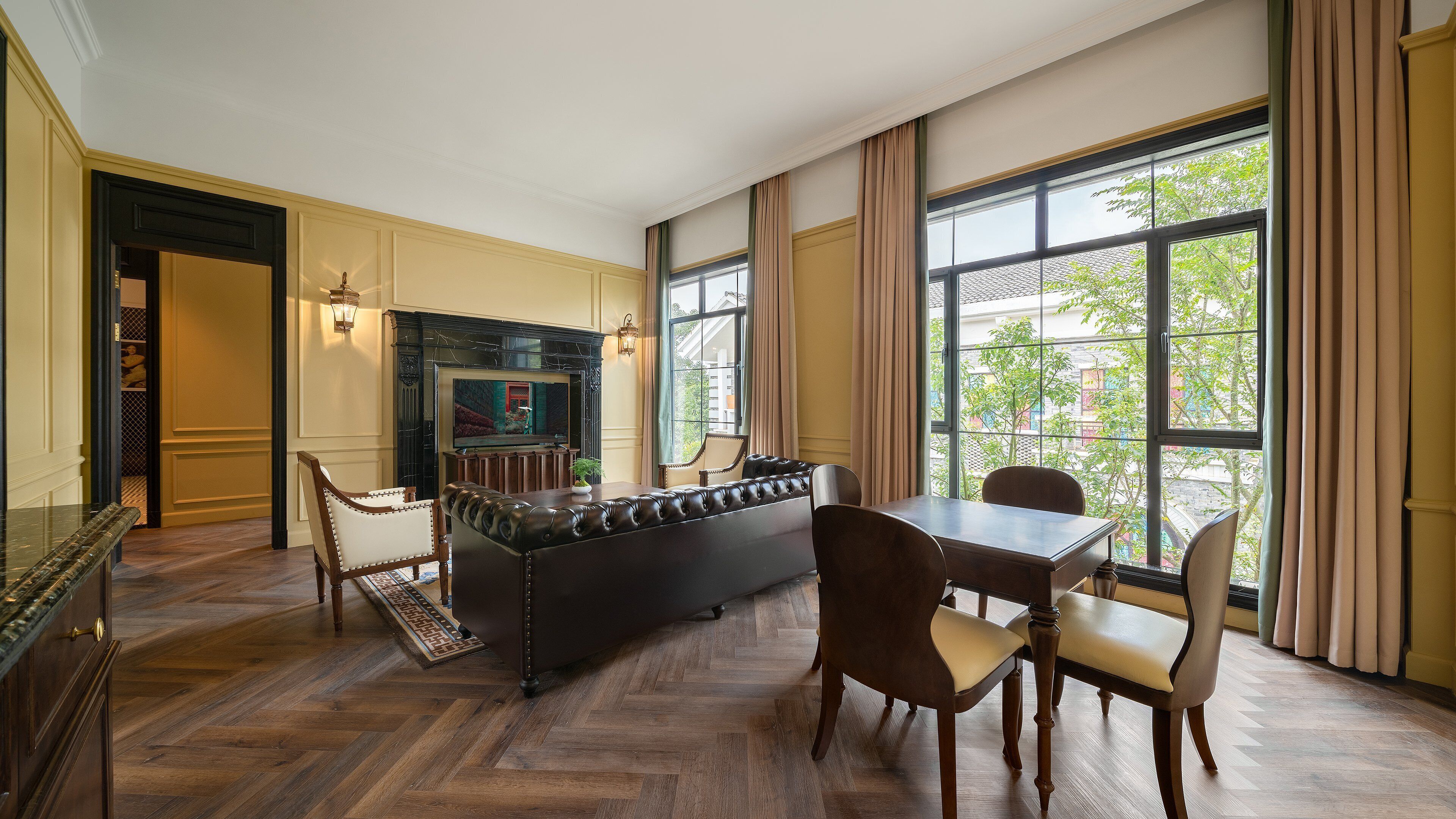 A dining area with a long table and chairs, a fireplace, and a view through large windows.