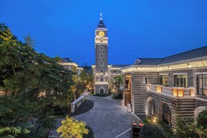 A traditional building with a clock tower, surrounded by lush greenery and a paved walkway.