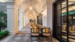 Un couloir doté d’un sol à carreaux, de colonnes blanches et d’une rangée de tables et de chaises.