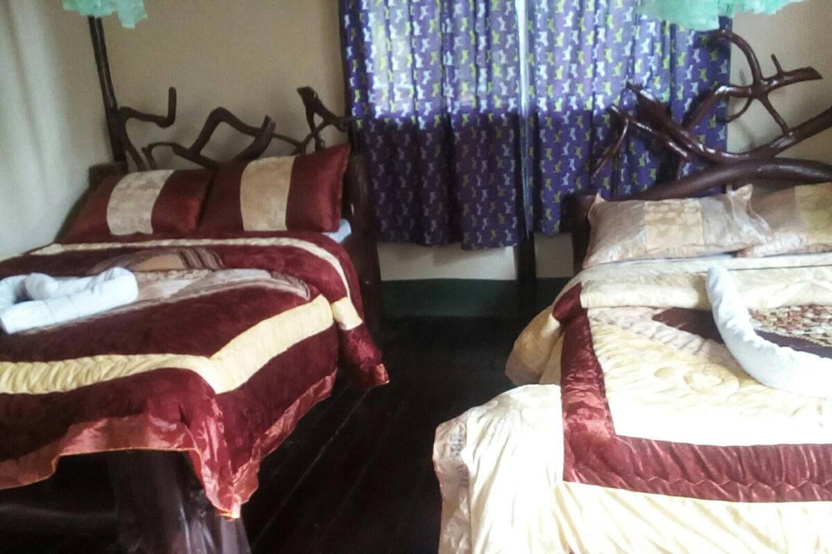 Duas camas com estruturas de madeira escura, cobertas com roupa de cama vermelha e bege.