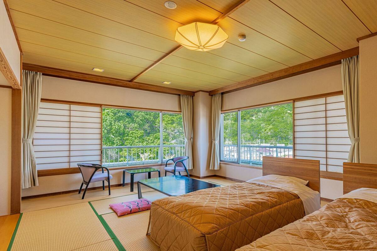 Een hotelkamer met twee bedden, een balkon met een tafel en stoelen, en grote ramen.
