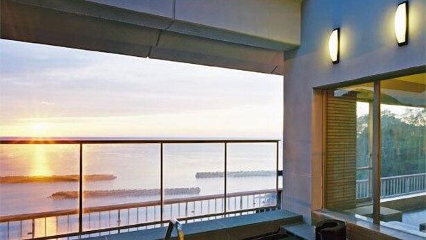 A modern outdoor pool area with a view of the sunset over water. - Izumatsuzaki Sou (Matsuzaki)