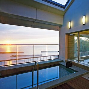A modern outdoor pool area with a view of the sunset over water. - Izumatsuzaki Sou (Matsuzaki)
