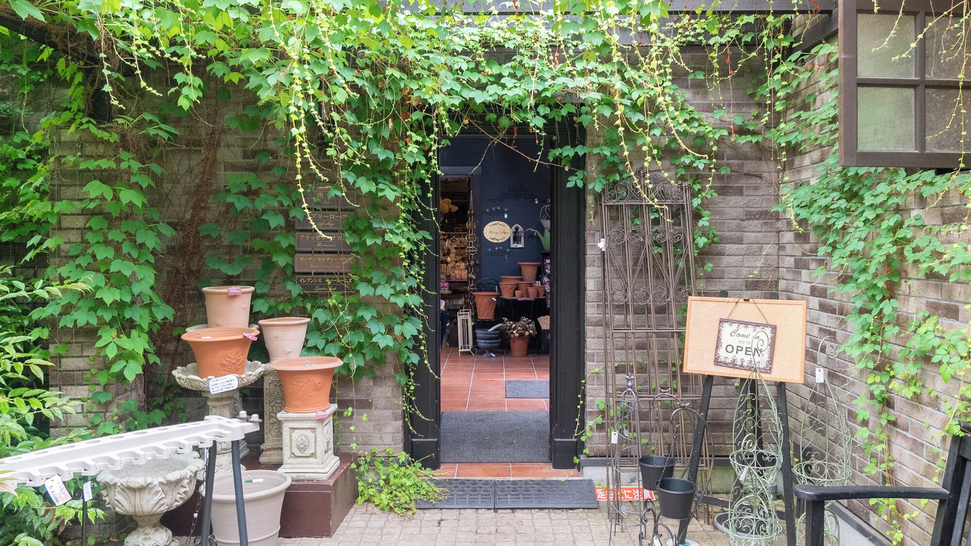 A brick building with a garden entrance, terracotta pots, and a signboard.