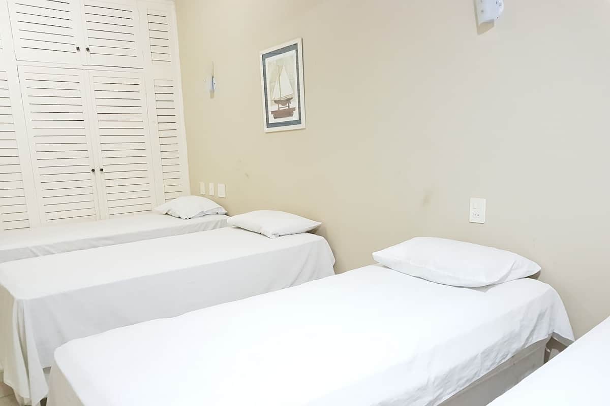 A room with two single beds, a white wall, a framed picture, and a white closet with louvered doors.