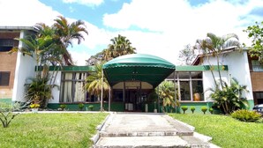 Un edificio con un ingresso sotto una tettoia verde, circondato da palme e un prato.