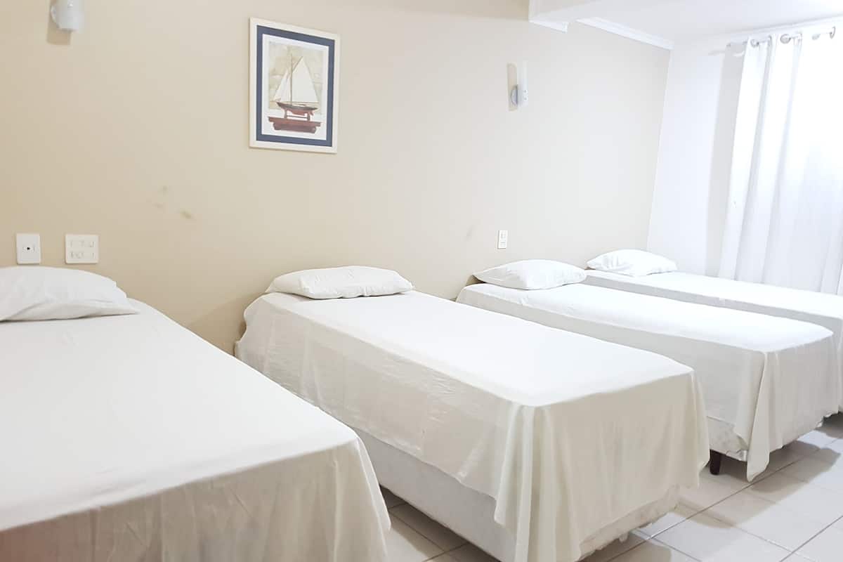 A hotel room with three single beds, a framed picture on the wall, and a window with curtains.