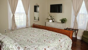 Une chambre à coucher avec un grand lit, une commode, un miroir, un téléviseur à écran plat et une chaise.
