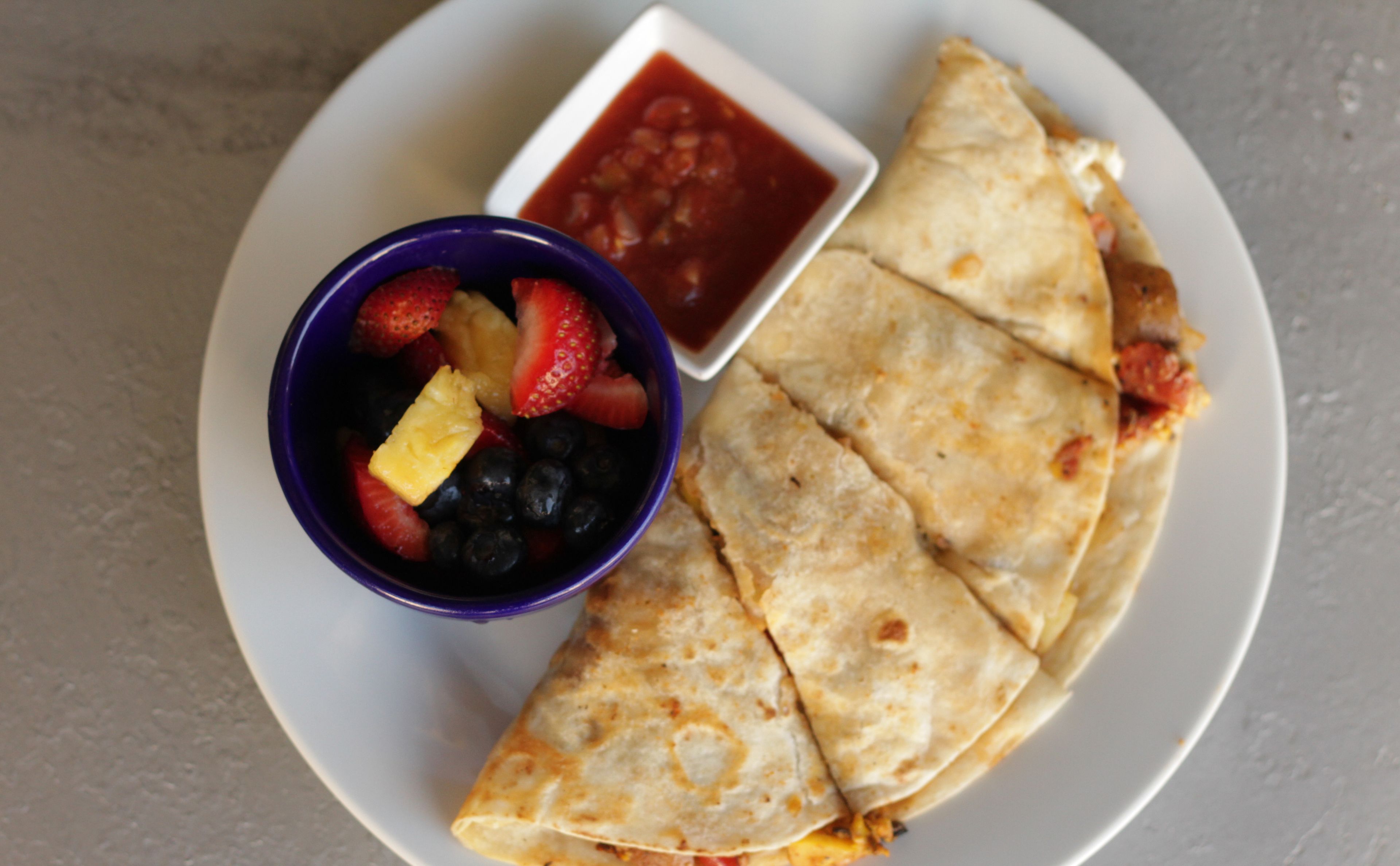 A plate with quesadillas and a bowl of fruit and salsa.