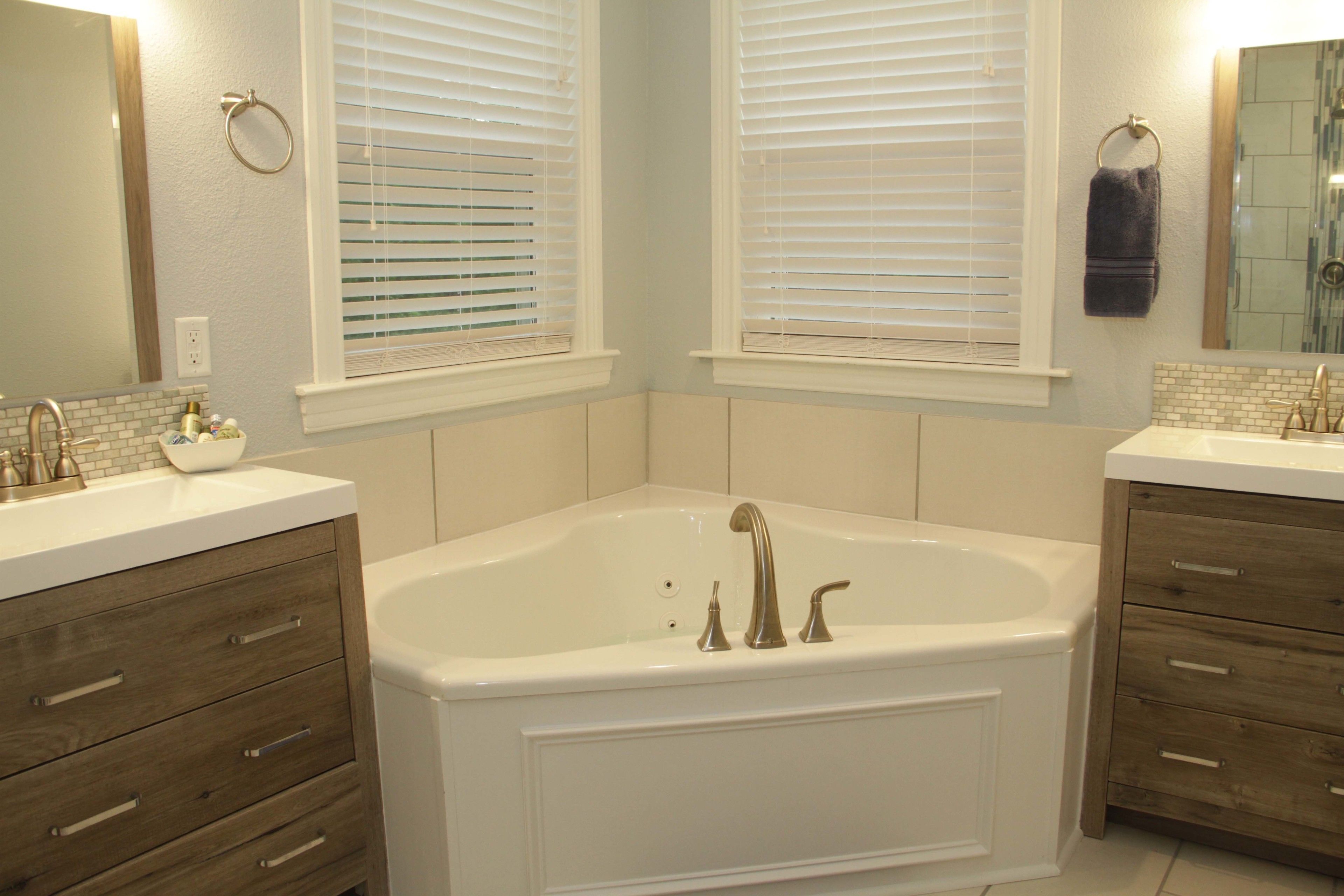 A bathroom with a large bathtub, two sinks, wooden cabinets, and a window with blinds.