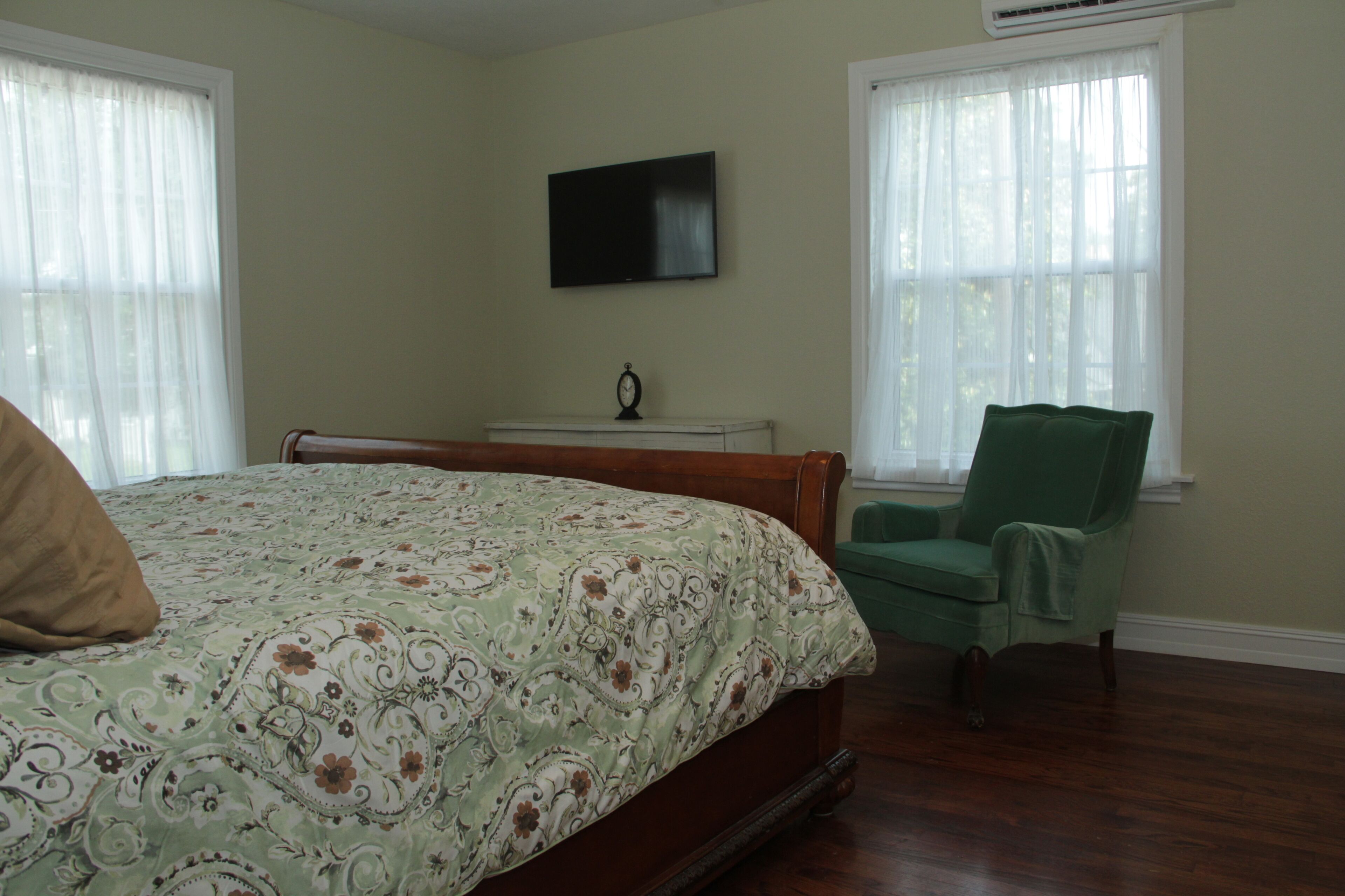 A bedroom with a bed, a chair, a TV, and a window.