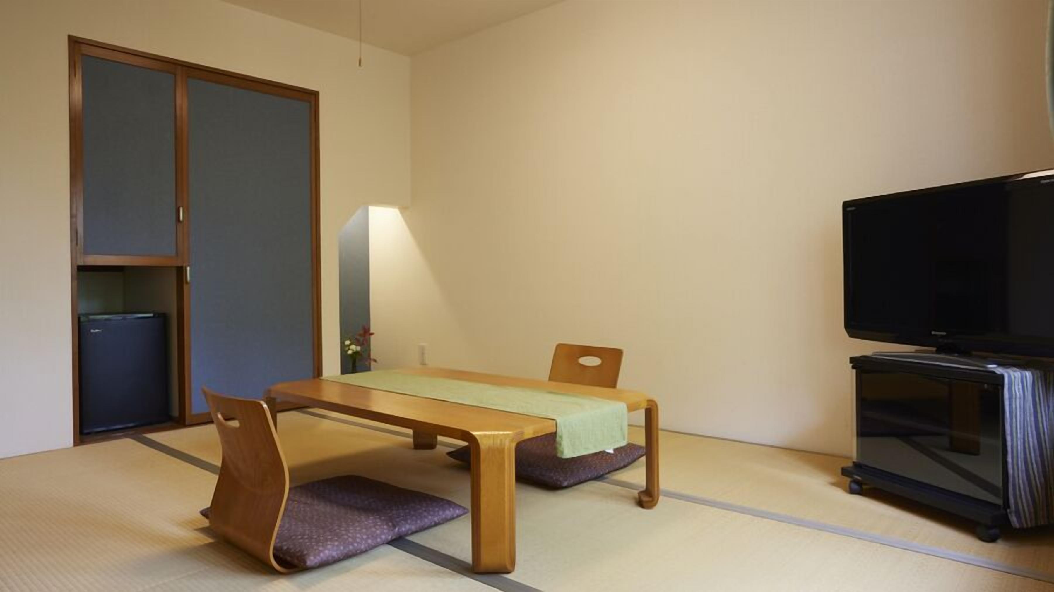Una habitación con suelo de tatami, una mesa baja con cojines, un televisor y un armario.