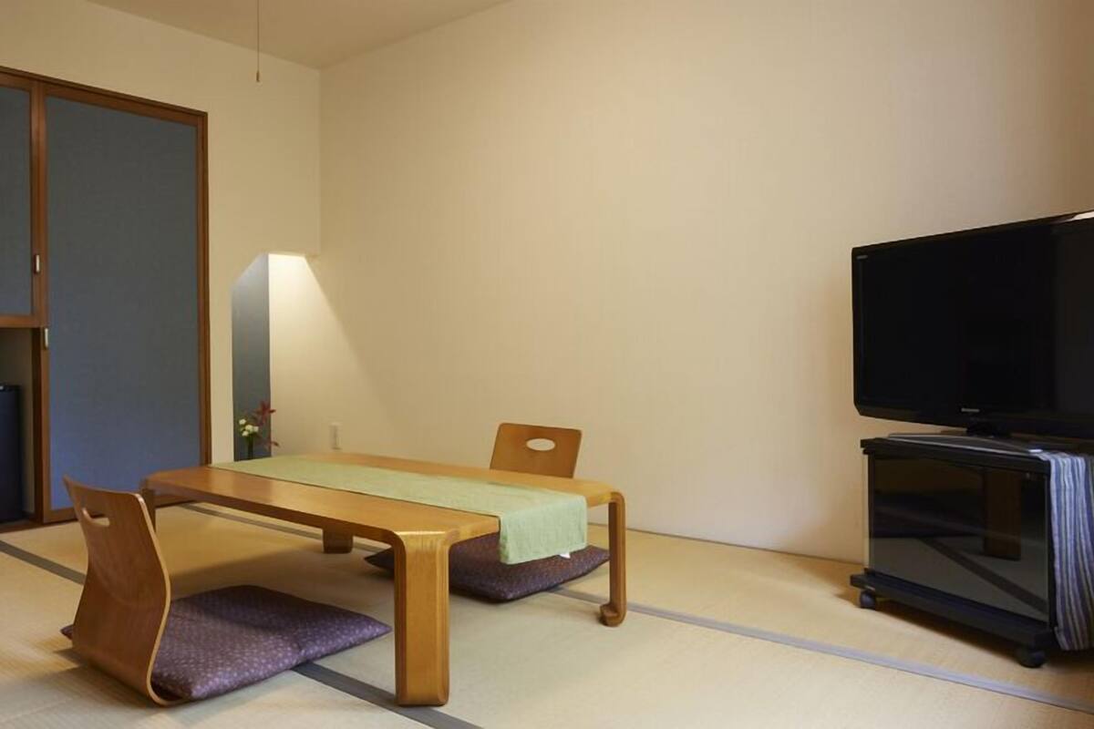 A room with tatami flooring, a low table with cushions, a television, and a cabinet.
