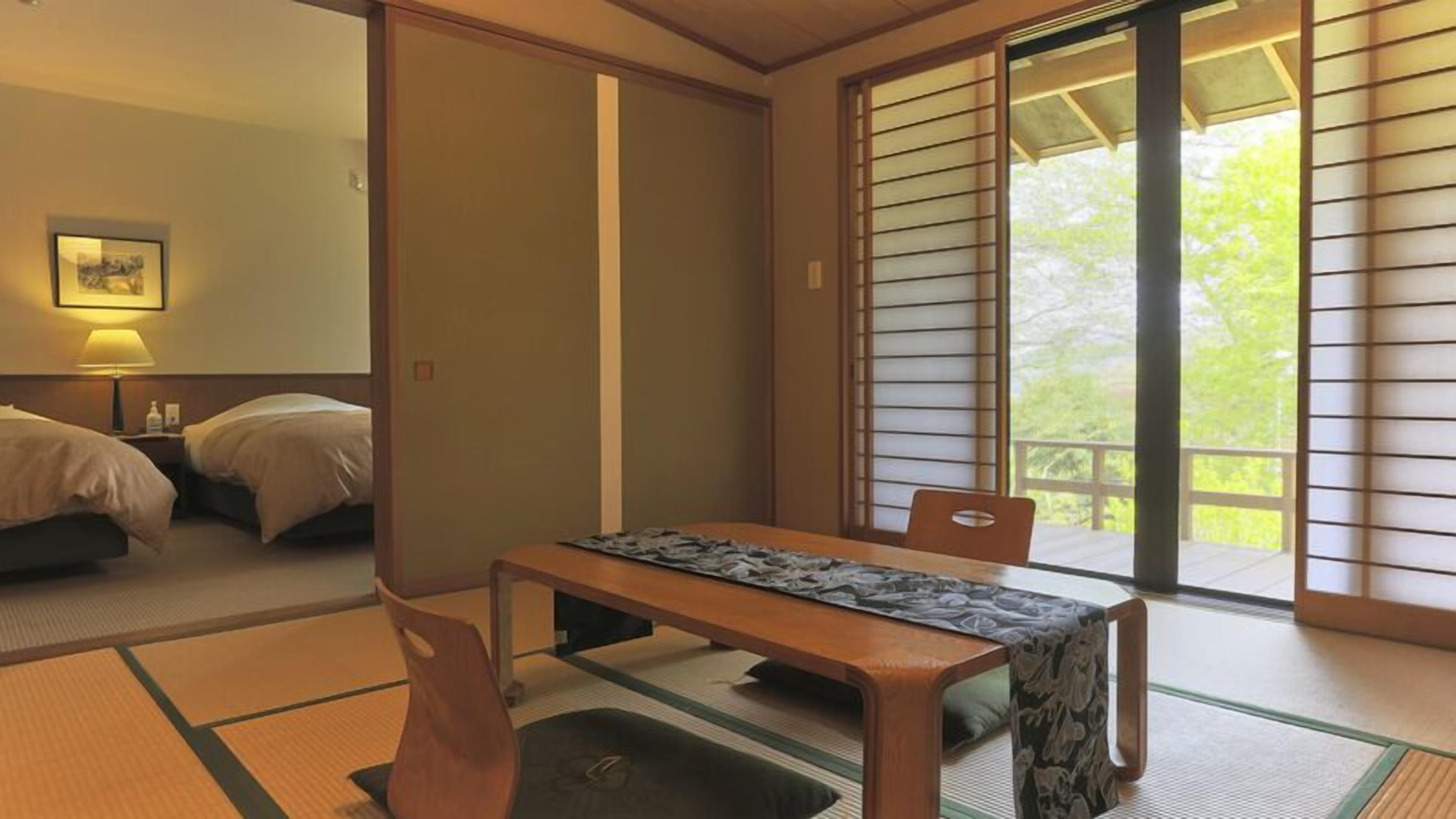 Una habitación japonesa tradicional con suelo de tatami, una mesa baja con mantel estampado, dos camas y una puerta corredera que da a un espacio exterior.