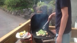 A person grilling outdoors with a grill and a plate of food. - Mastlamp (Ito)