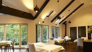 A modern dining area with tables set for two, large windows, and a high ceiling with exposed beams. - Mastlamp (Ito)