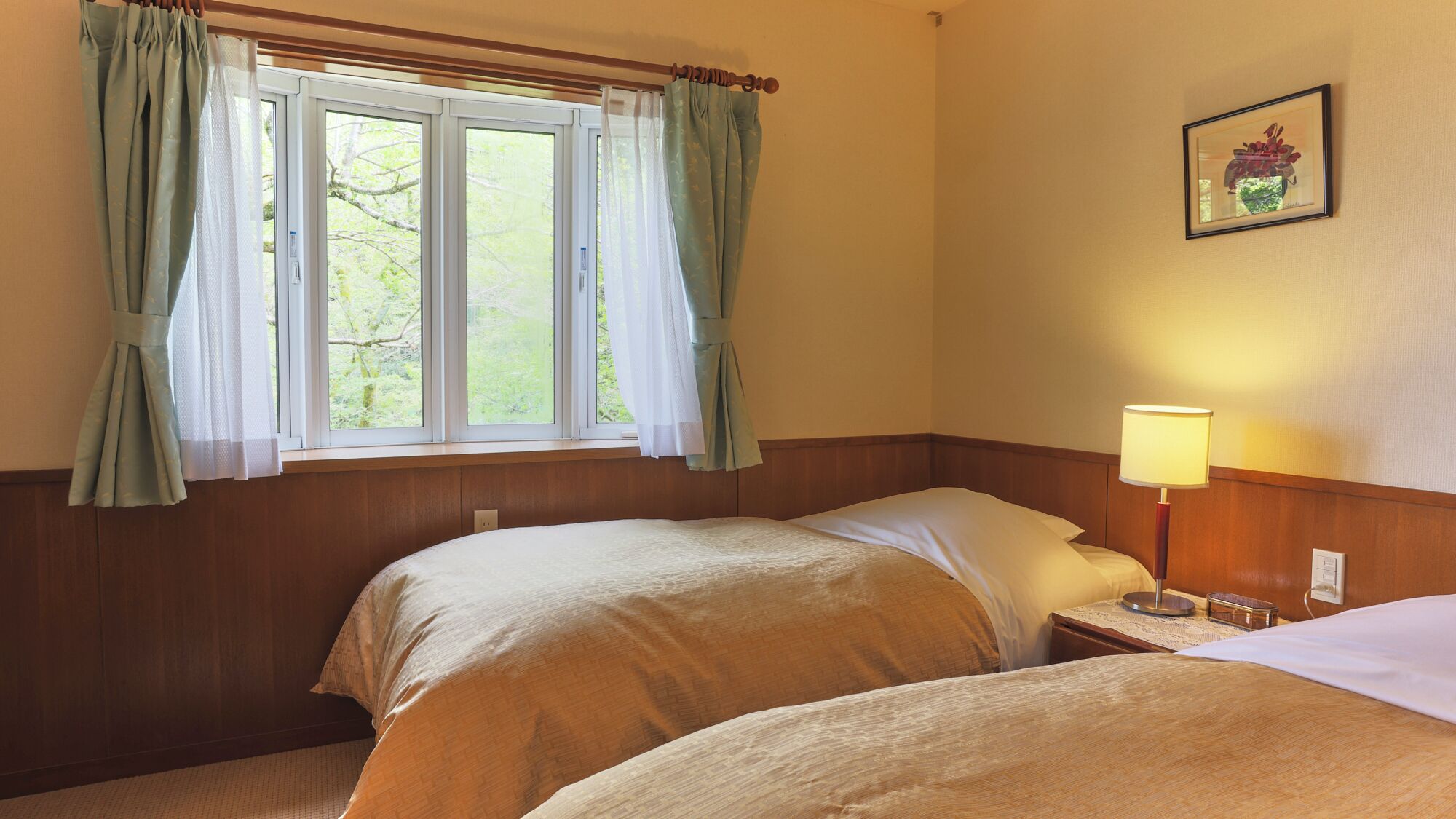 Una habitación con dos camas, una ventana con cortinas, una lámpara de noche y un cuadro en la pared.