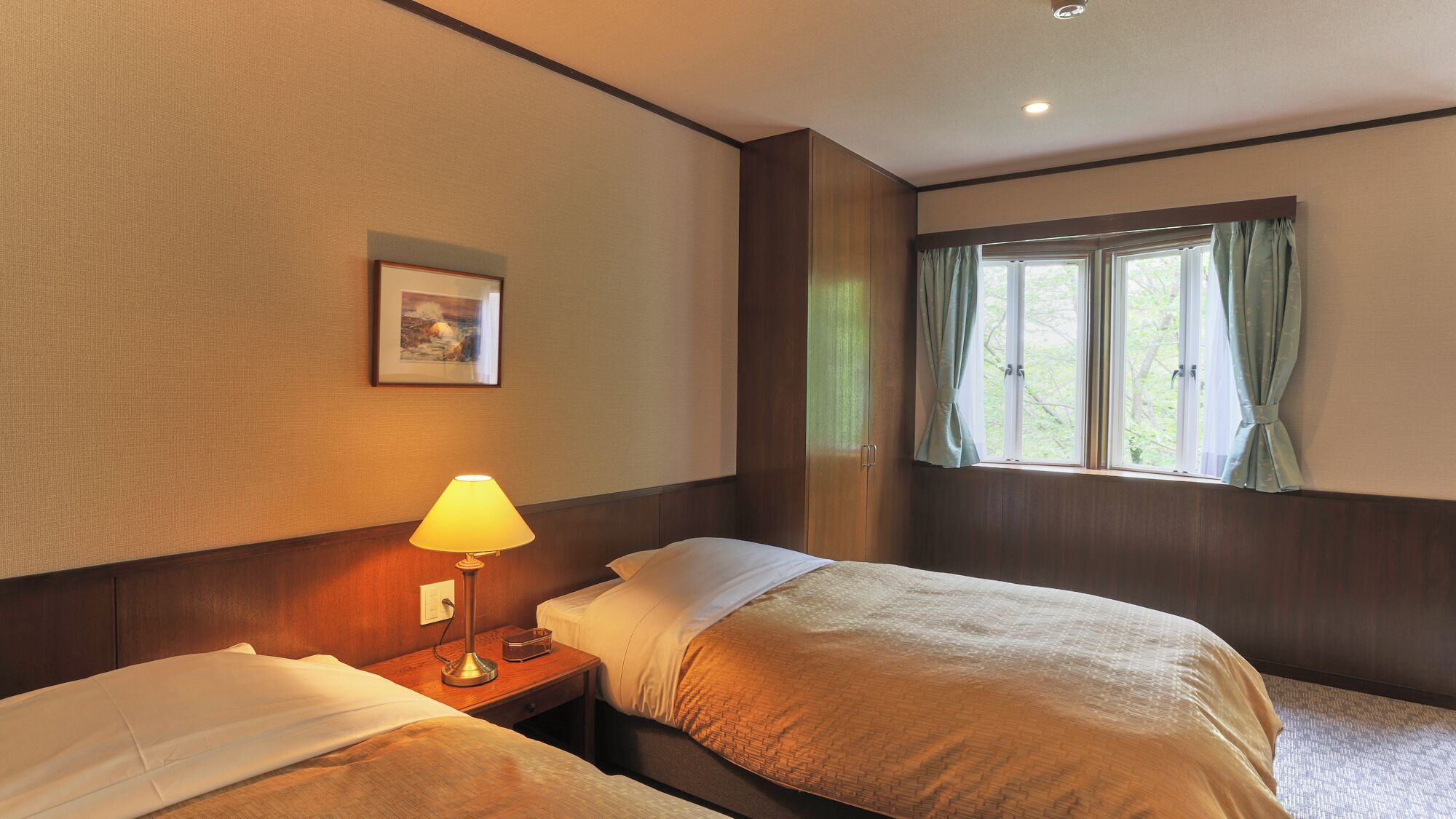 Habitación de hotel con dos camas, una lámpara de noche, una ventana con cortinas y un cuadro en la pared.