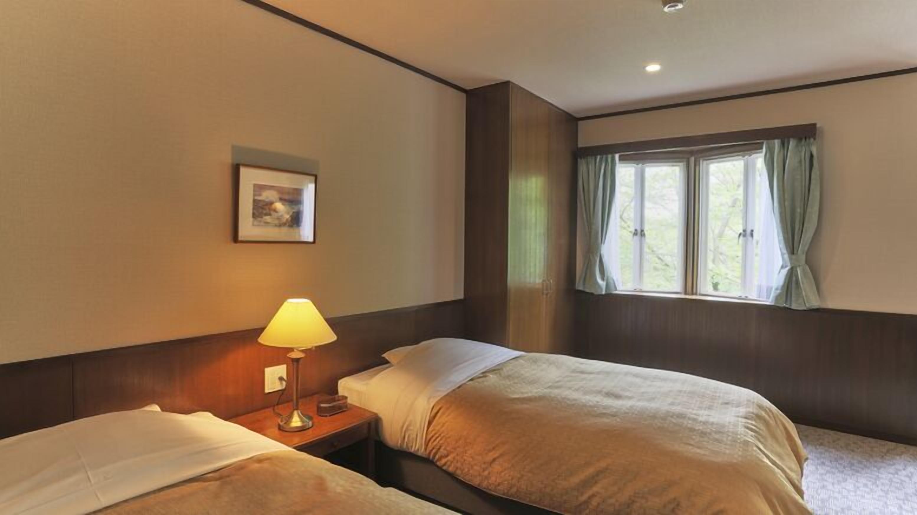 Habitació d'hotel amb dos llits, una làmpada de nit, un quadre al mur i una finestra amb cortines.