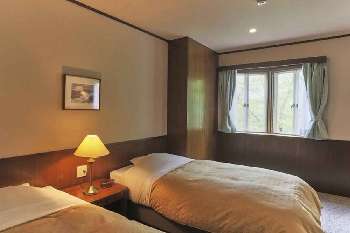 A hotel room with two beds, a bedside lamp, a framed picture on the wall, and a window with curtains.