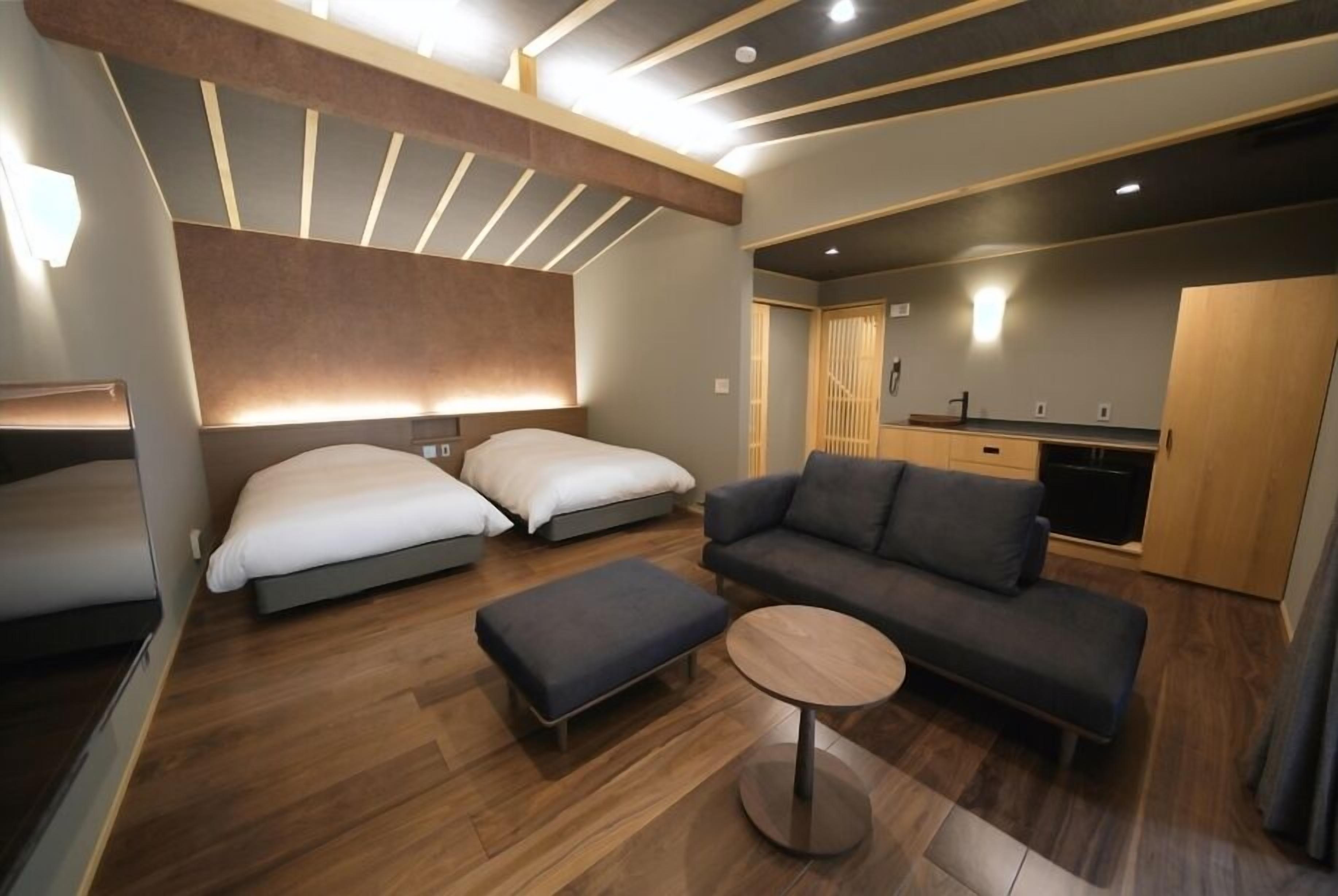Habitació d'hotel moderna amb sofà, dos llits, taula petita i cuina sencera.