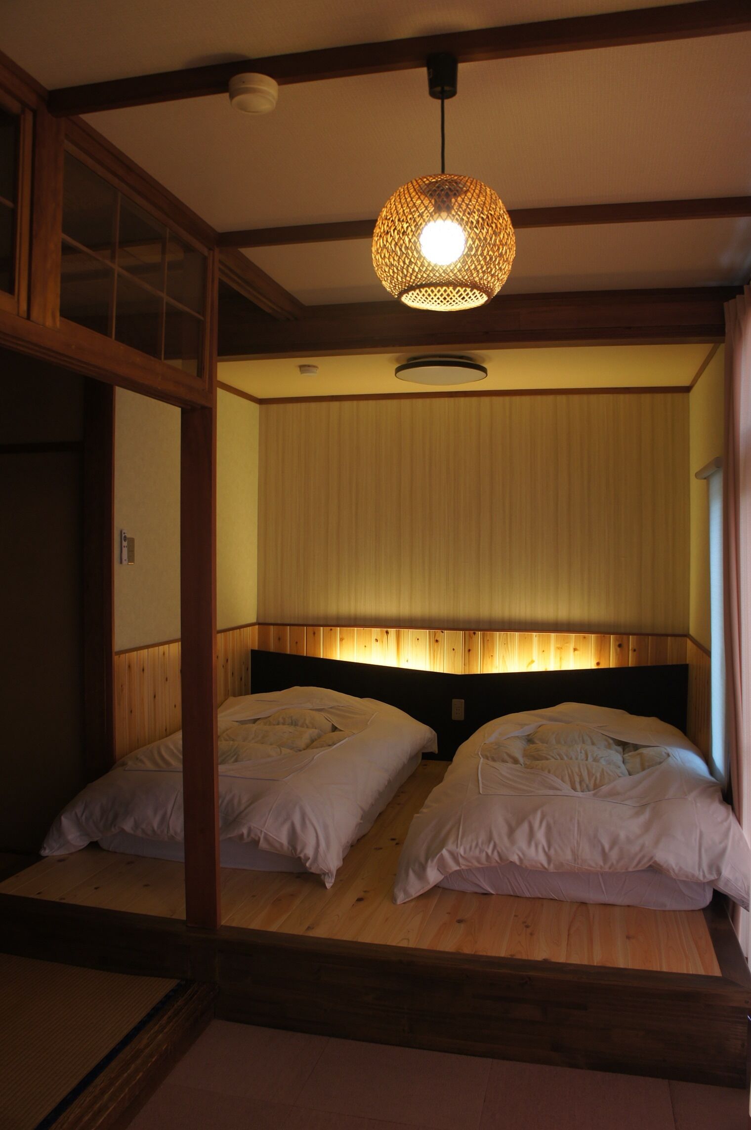 Una habitación tradicional japonesa con dos camas, un futón de tatami y una lámpara colgante.