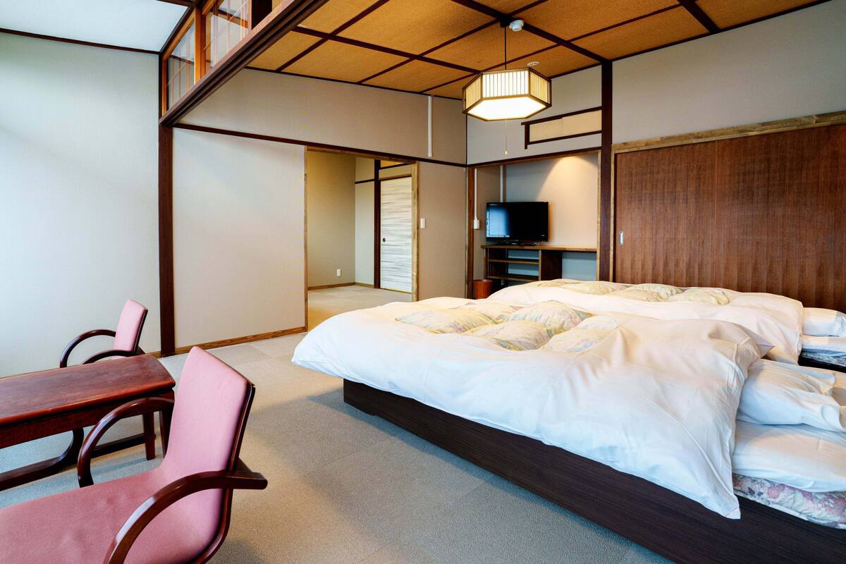 A bedroom with a bed, a TV, a desk, and chairs.