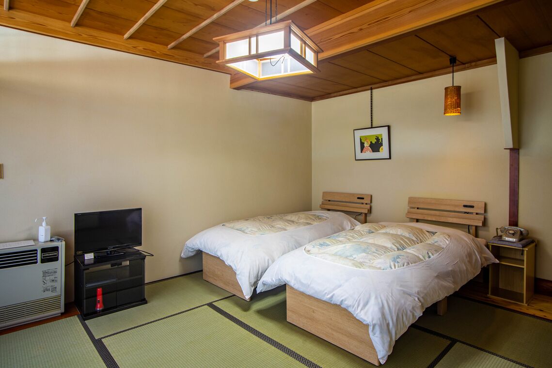 A room with two beds, a television, a heater, and a picture on the wall.