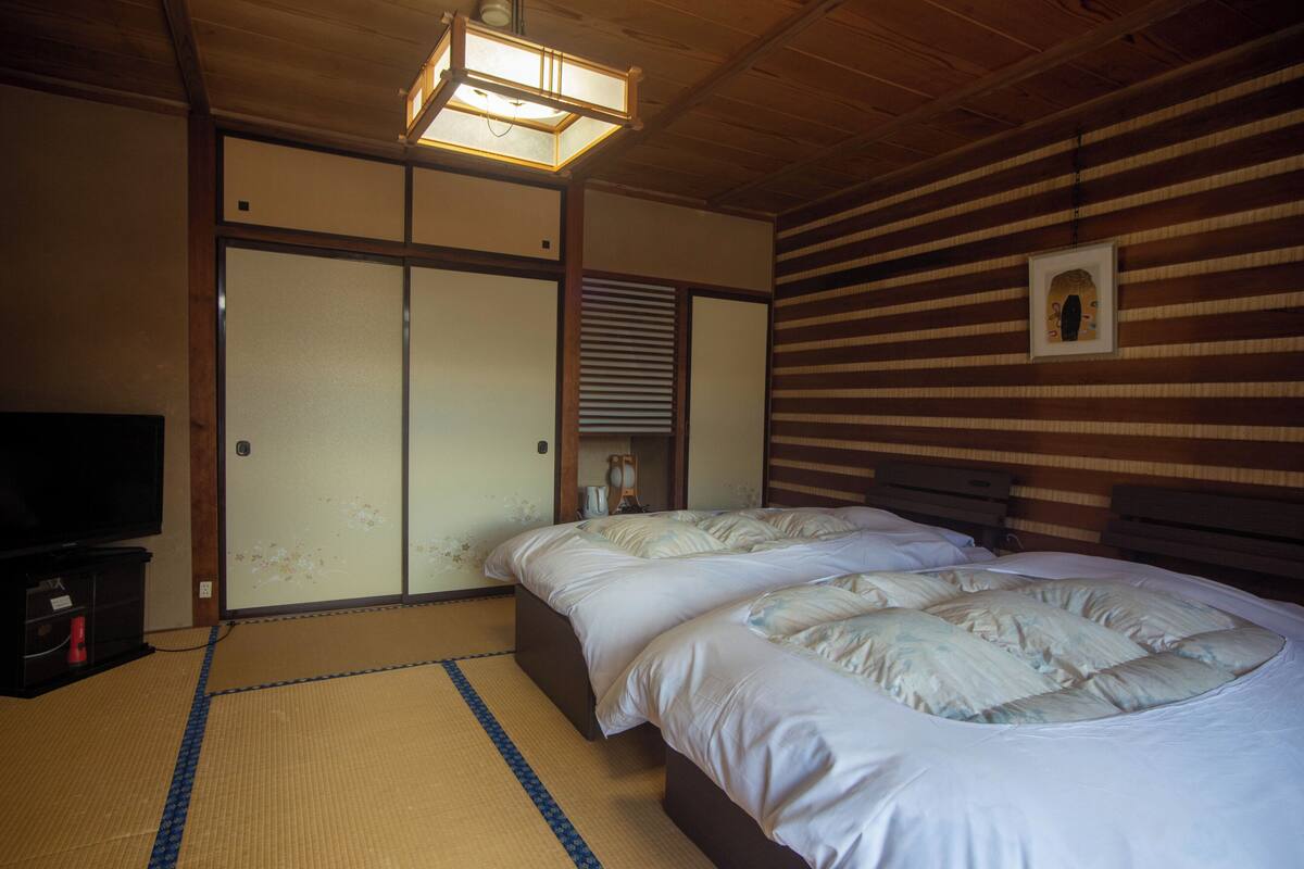 A traditional Japanese room with tatami flooring, two beds, a television, and sliding doors.
